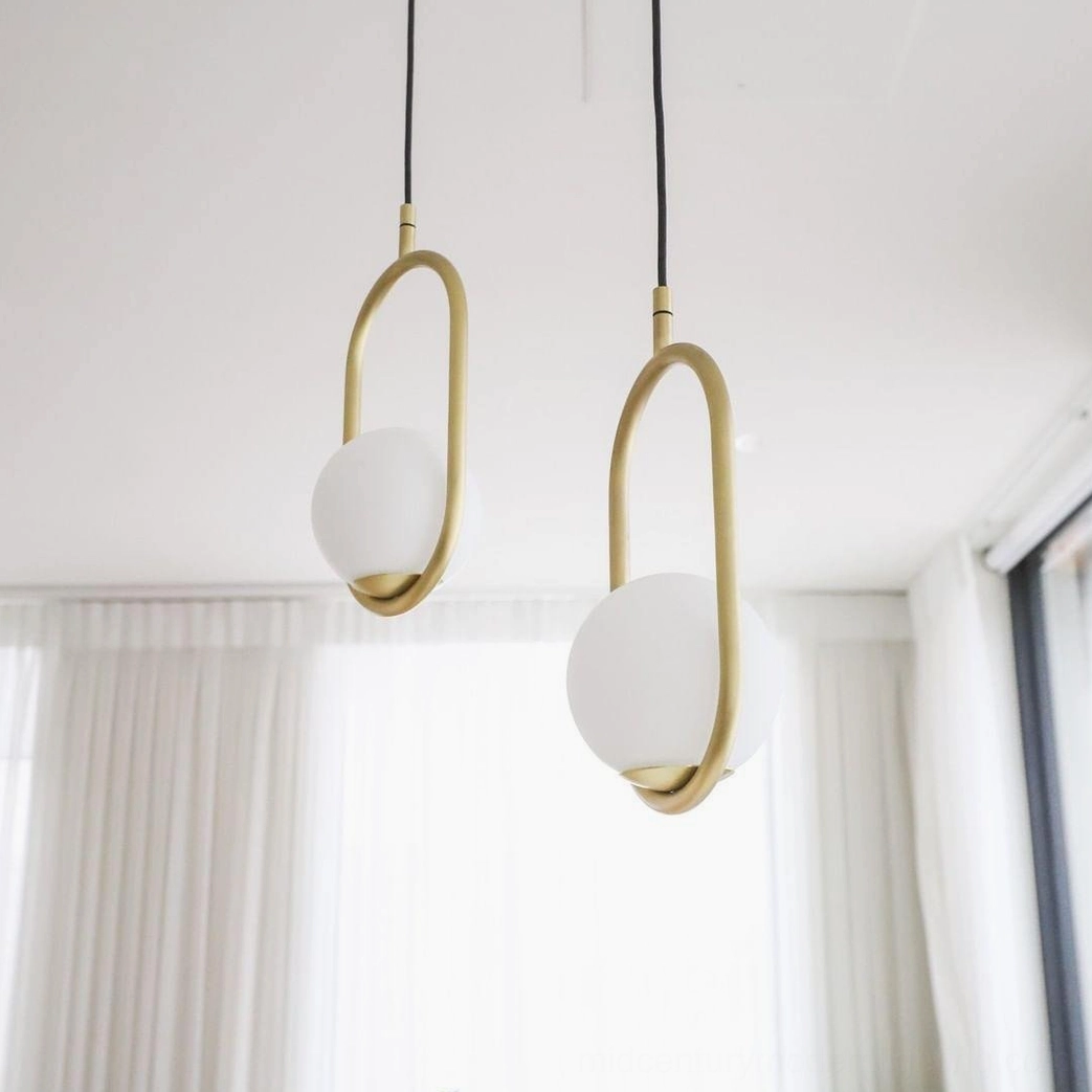 Mila oval frosted glass pendant light with brass fixture by sunlit window, minimalist modern interior lighting with natural light