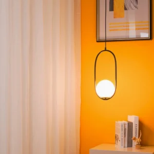 Mila oval frame pendant light in black metal with warm glass globe shade suspended in modern living room with orange accent wall