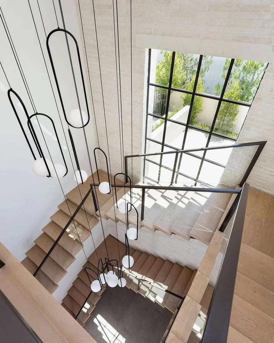 Overhead view of Mila pendant light cluster installed in modern stairwell with black metal frames and white glass orbs