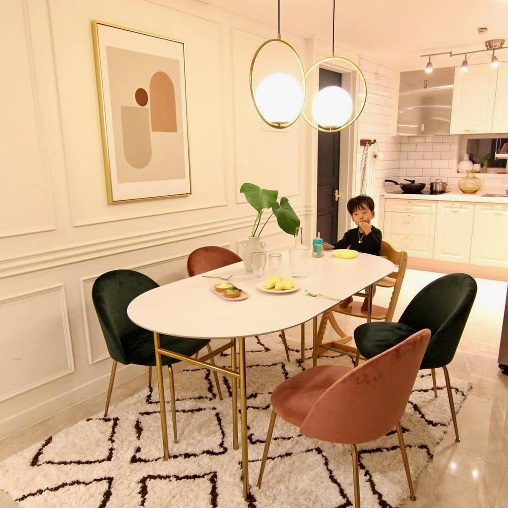 Two Mila pendant lights hanging in warm residential dining room with mixed color chairs, mid-century modern brass glass lamp fixtures