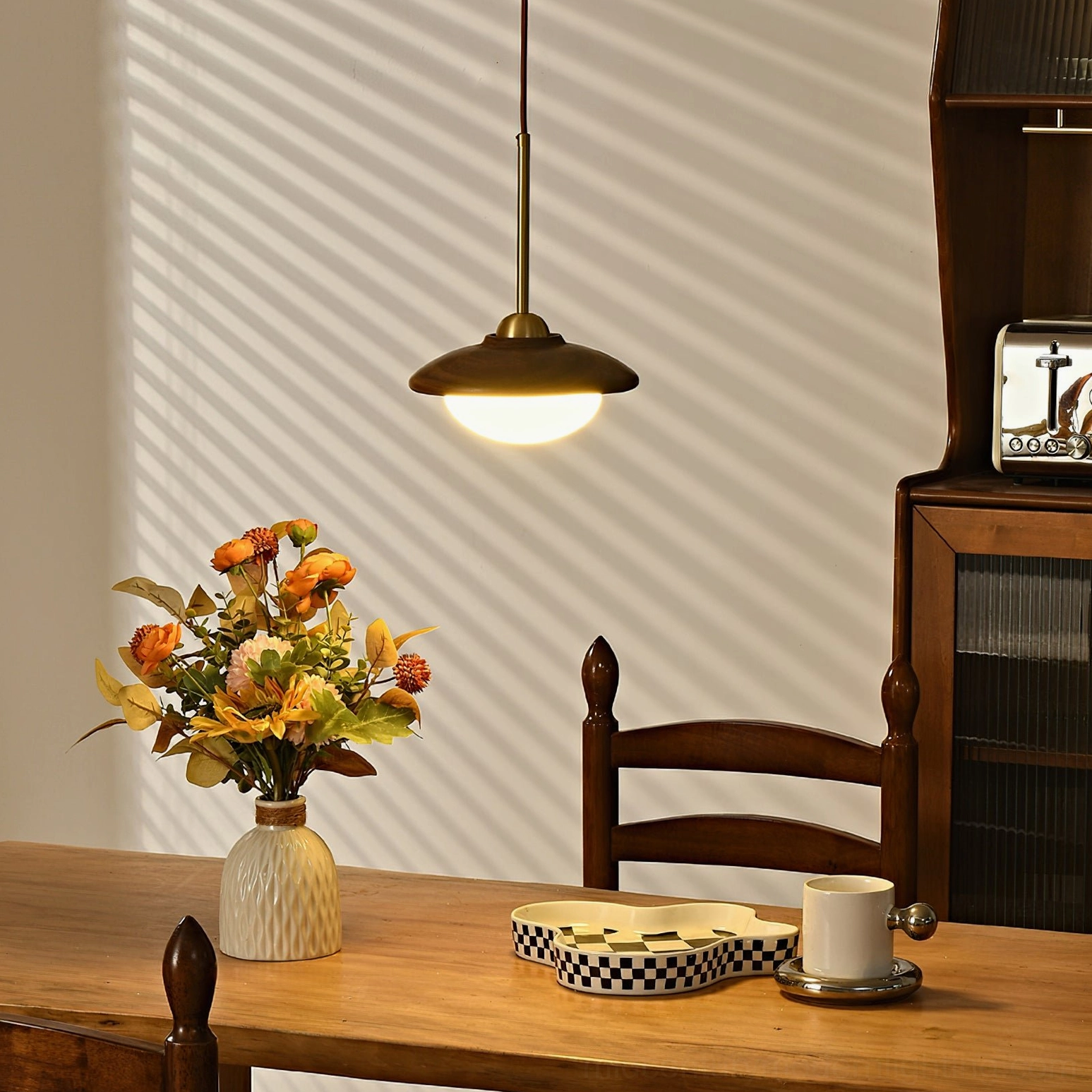 Milivia single pendant light in dining room casting warm shadows on wall - side view