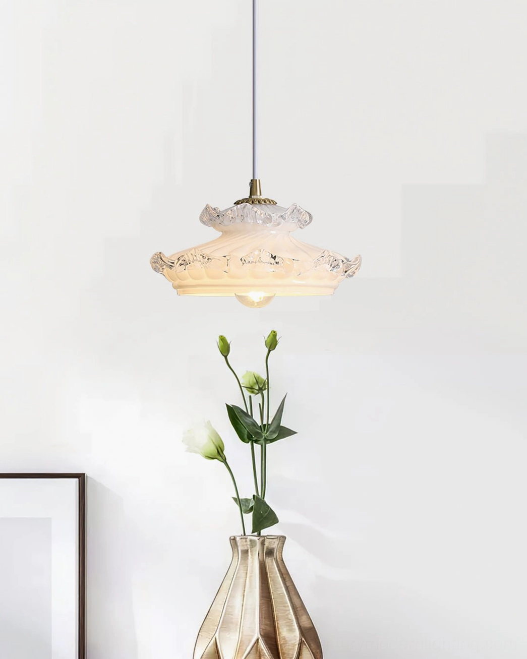 Off-white milk glass pendant light with brass suspension hardware beside decorative flower vase