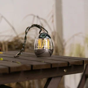 Mini Egg LED camping lamp glowing warm light on outdoor wooden picnic table with dry grass backdrop