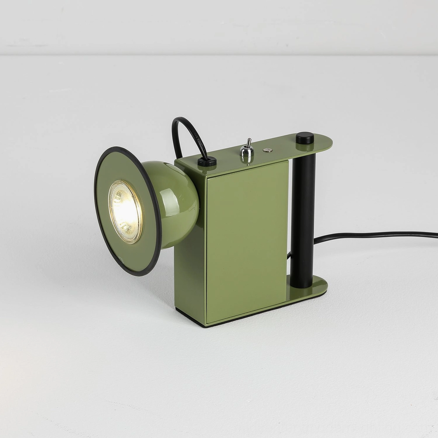 Sage green Minibox industrial table lamp, three-quarter view with lit spotlight head, studio photography