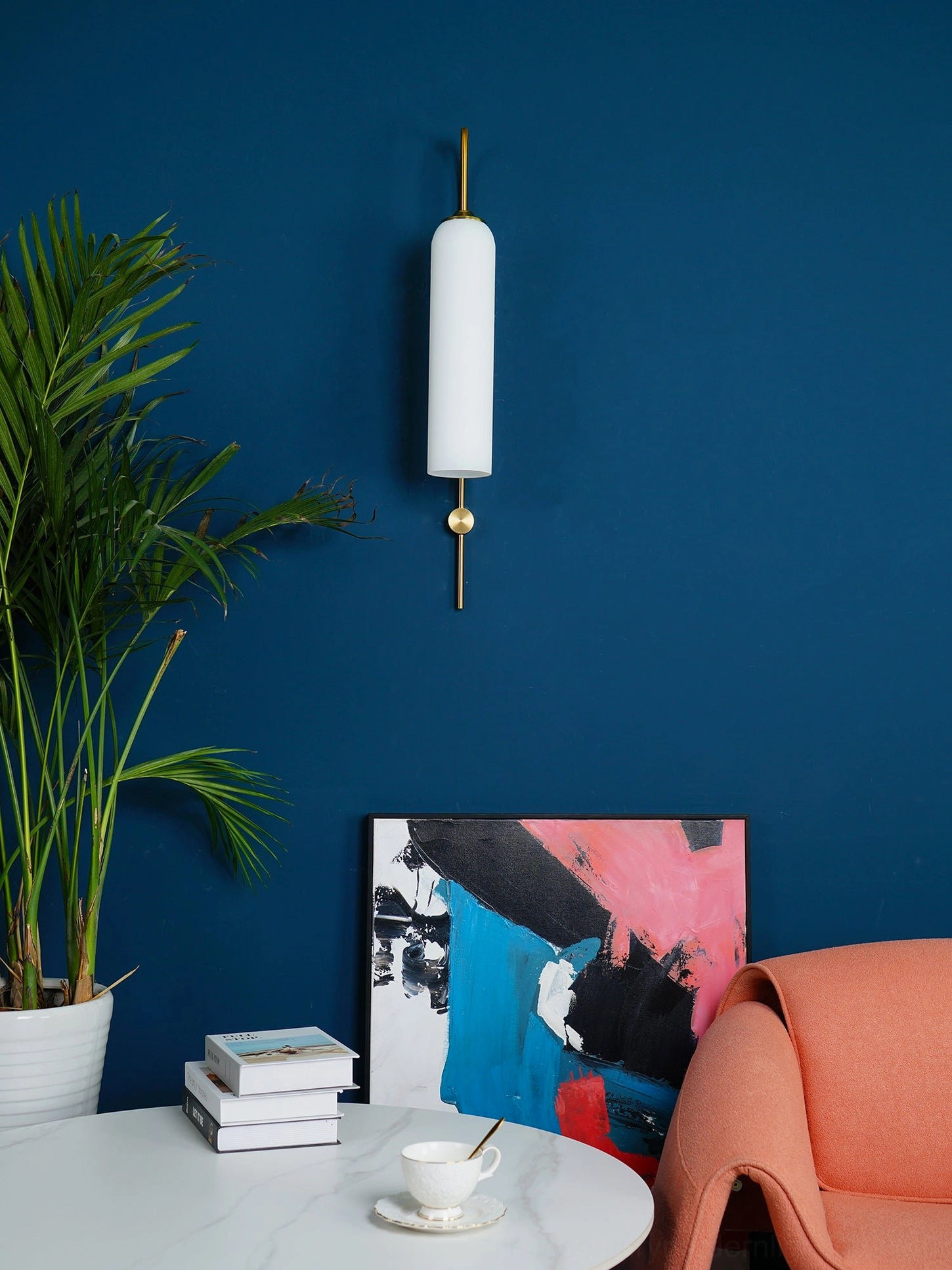Modern cylindrical wall sconce with straight brass rod and small gold round accent on dark blue background