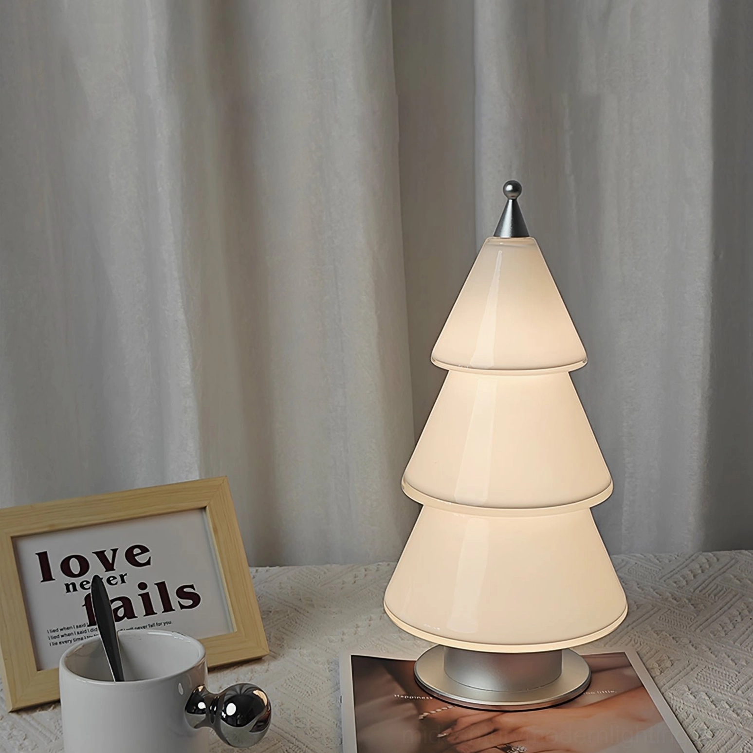 Geometric tiered cone LED lamp with silver metal details on minimalist desktop with curtain background
