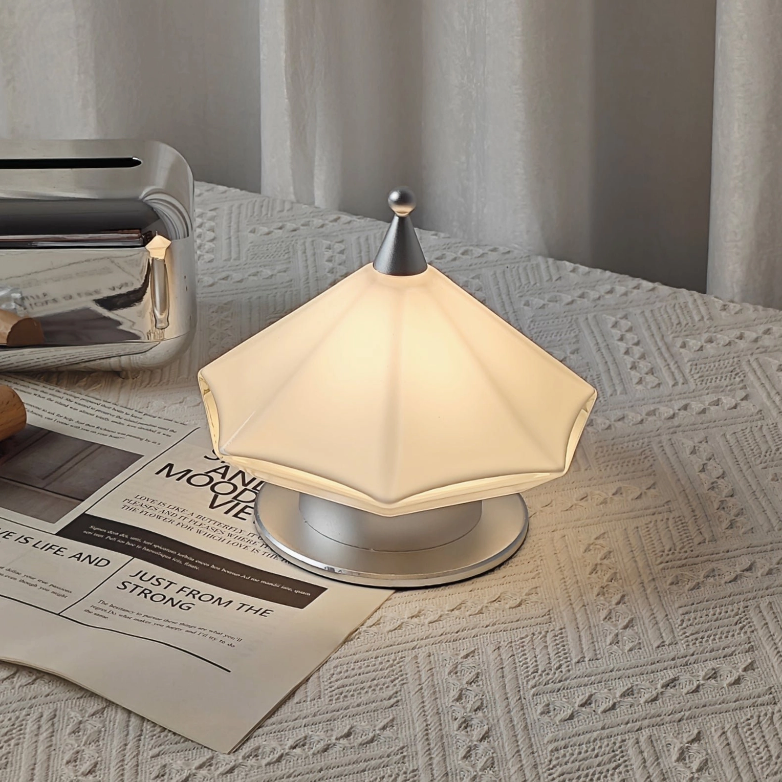 Faceted cone-shaped table lamp with white acrylic layered shade overhead flat lay on linen textured bedside surface