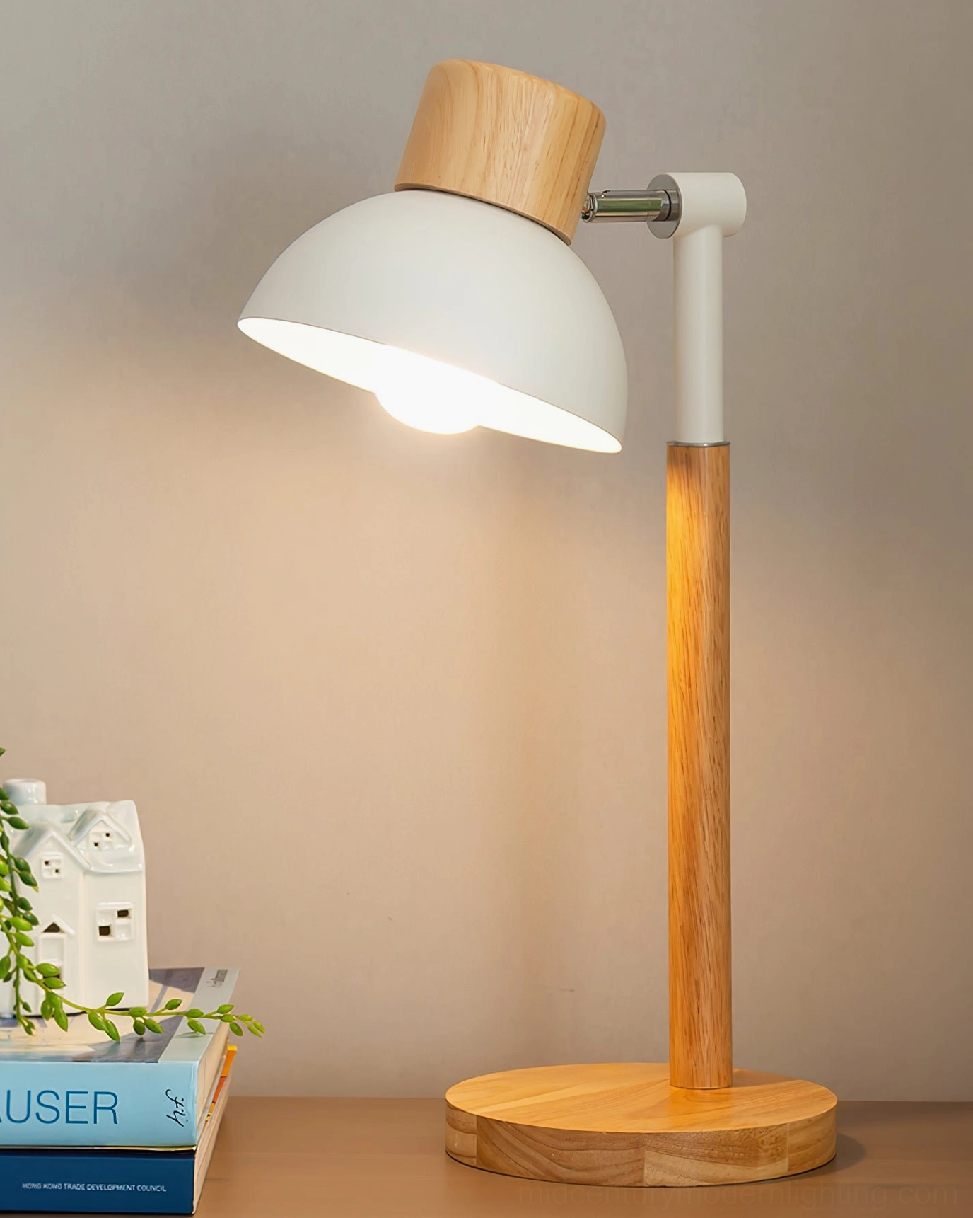Small Nordic desk lamp with tilted white shade casting warm glow on wooden work surface