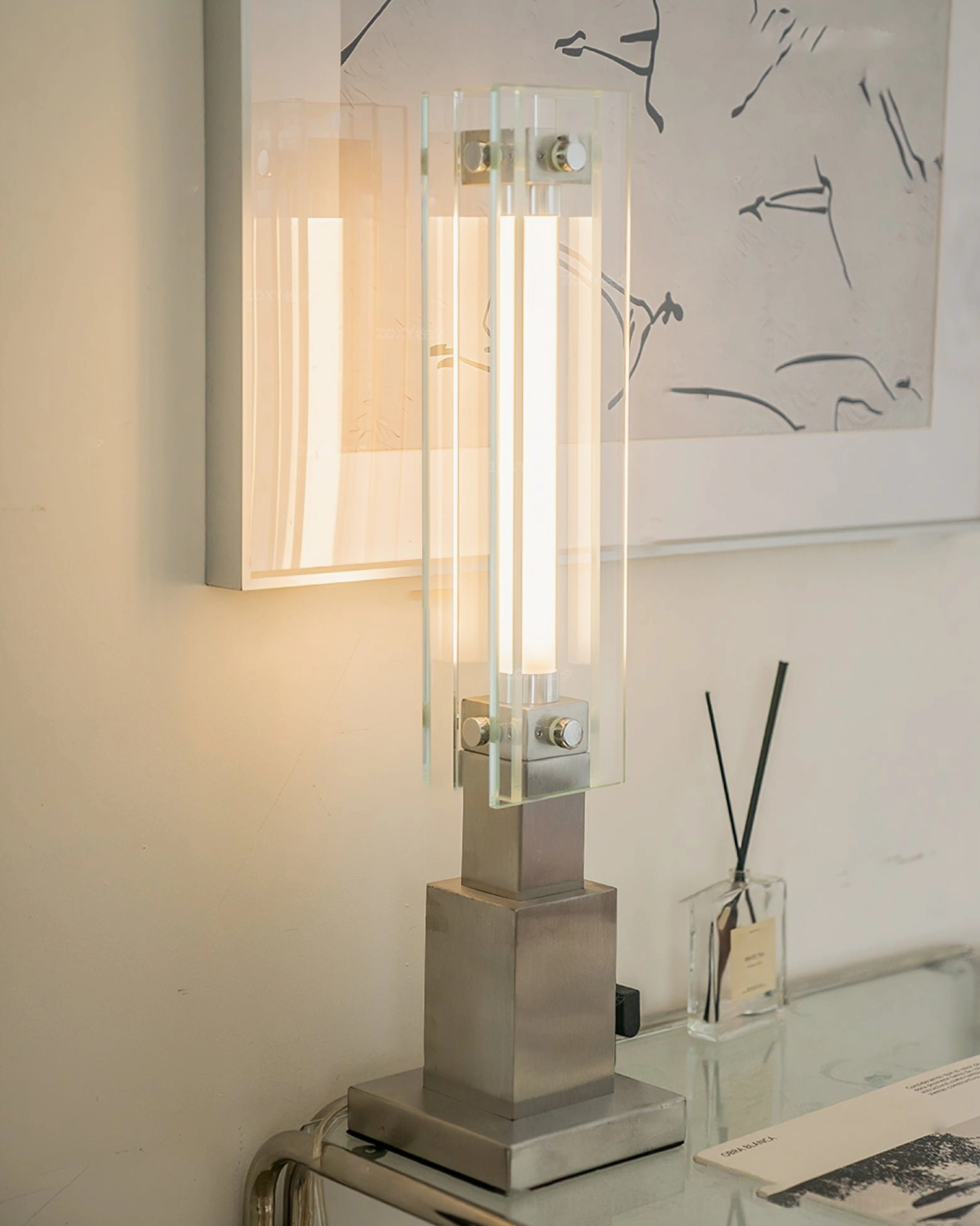 Sleek glass cylinder lamp on glass-top dressing table with reed diffuser home decor styling