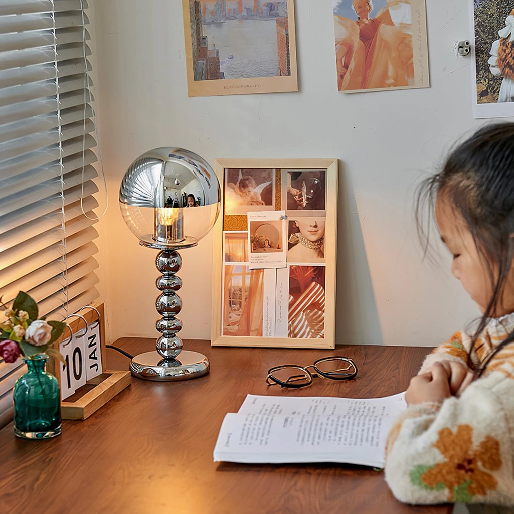 Illuminated chrome Mirrorball table lamp glowing on home study desk workspace with Edison bulb visible
