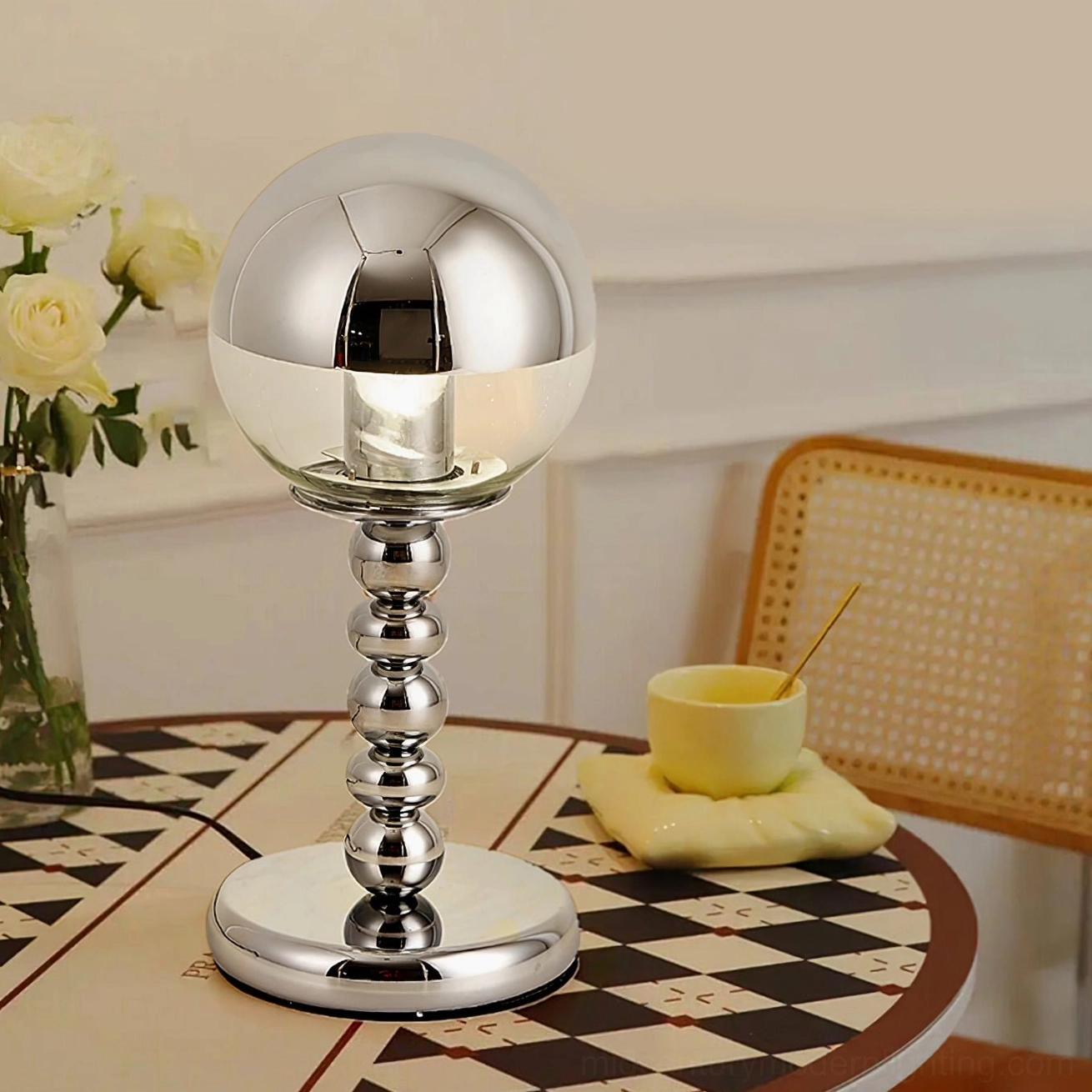 Reflective chrome Mirrorball lamp on checkered round dining table with floral vase and yellow coffee cup