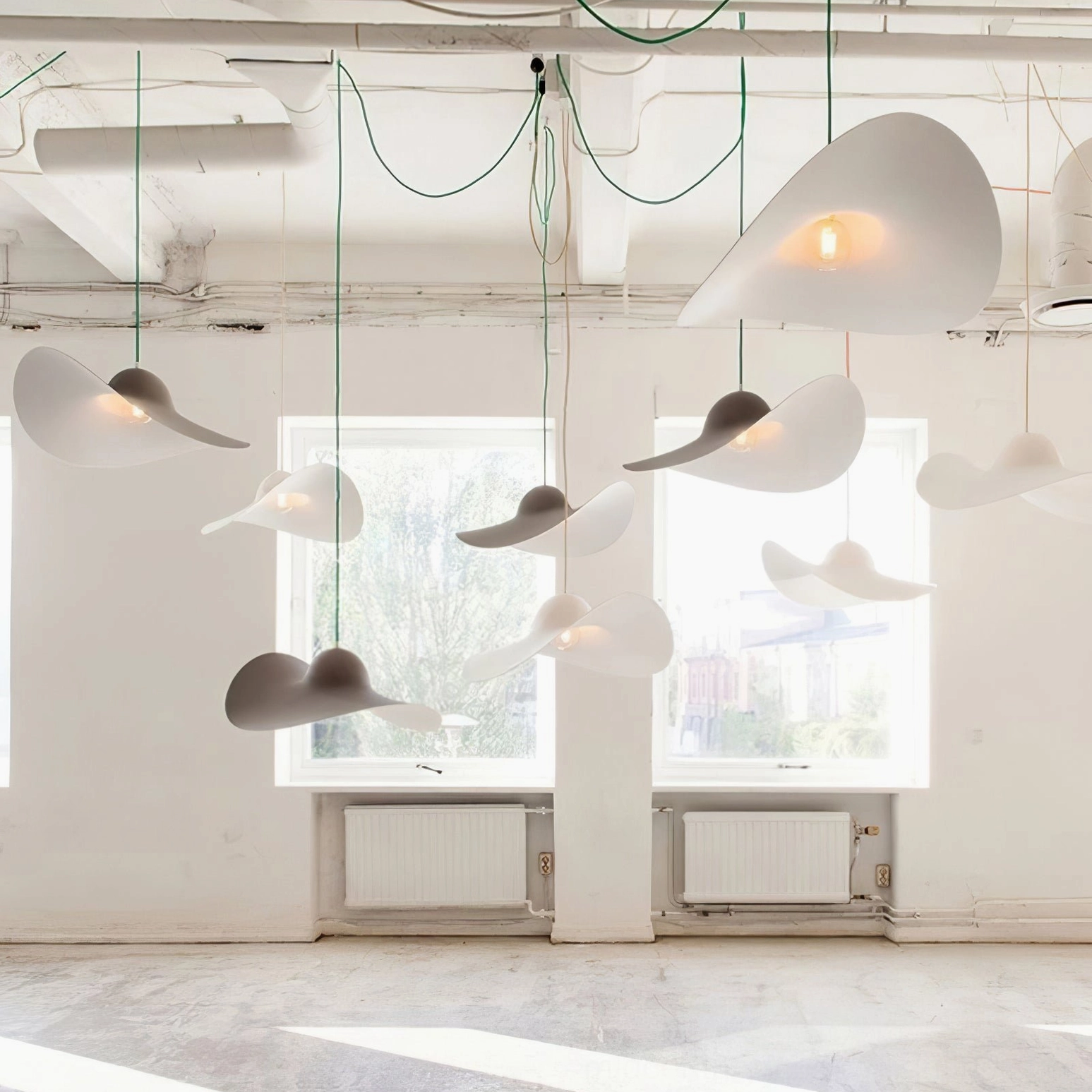 Multiple assorted hat pendant lamps in white and gray hung in bright industrial loft space
