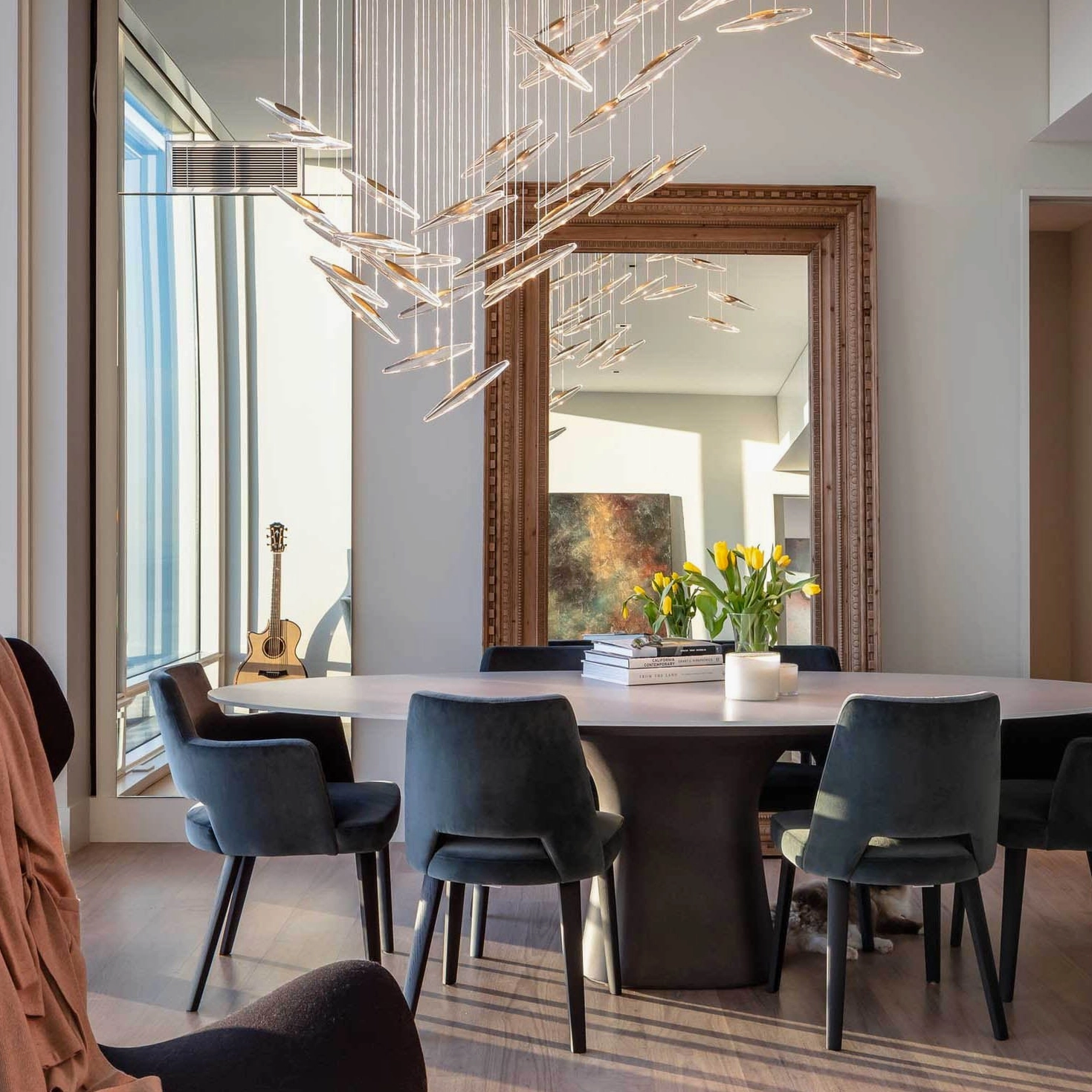 Modern cascading glass chandelier with warm lighting above round dining table and wall mirror in bright dining area