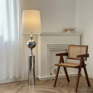 Articulated chrome floor lamp in contemporary living room setting with fireplace, wooden chair, and natural light through sheer curtains