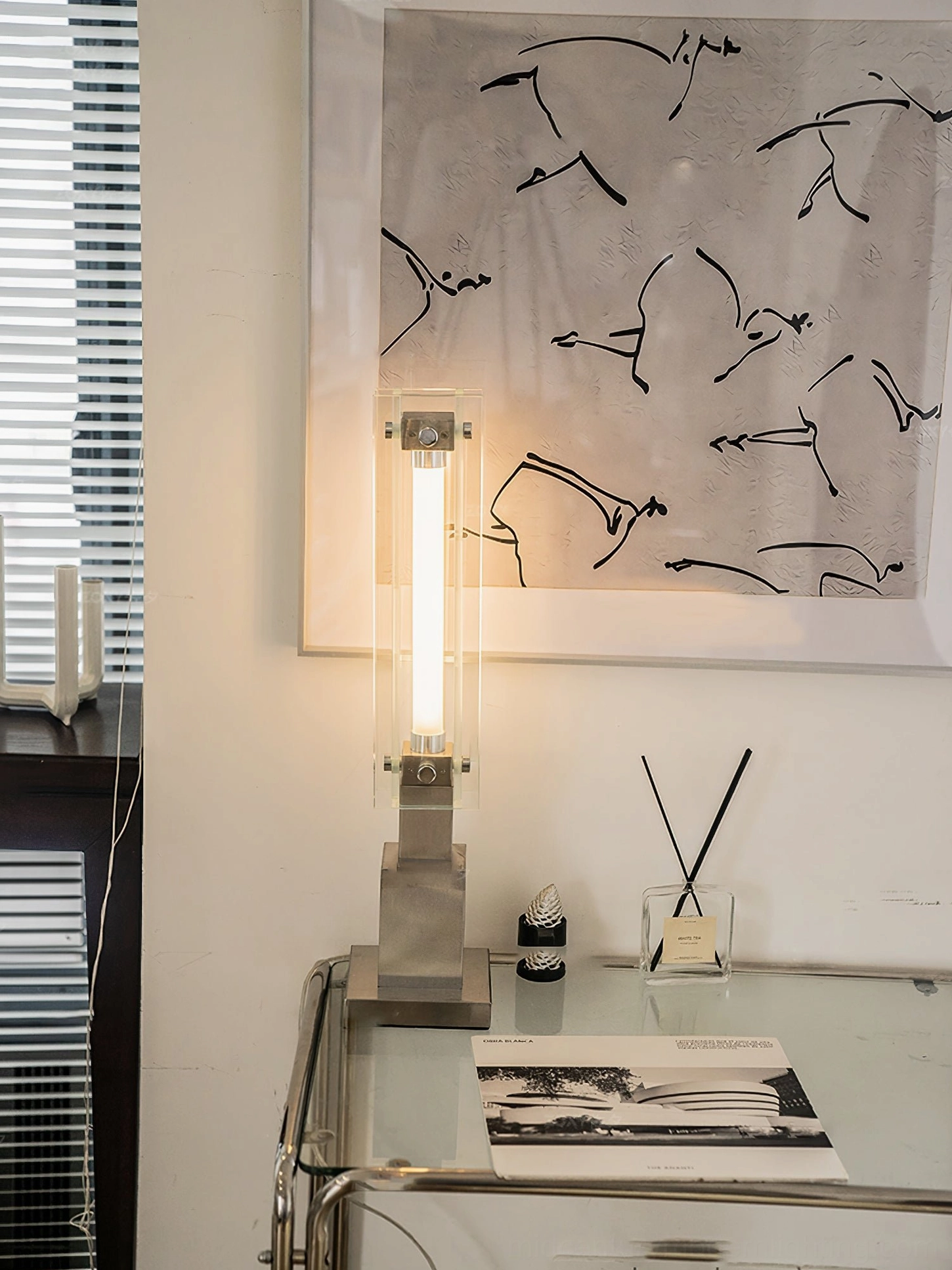 Chrome and glass modern lamp positioned by window blinds in neutral home workspace