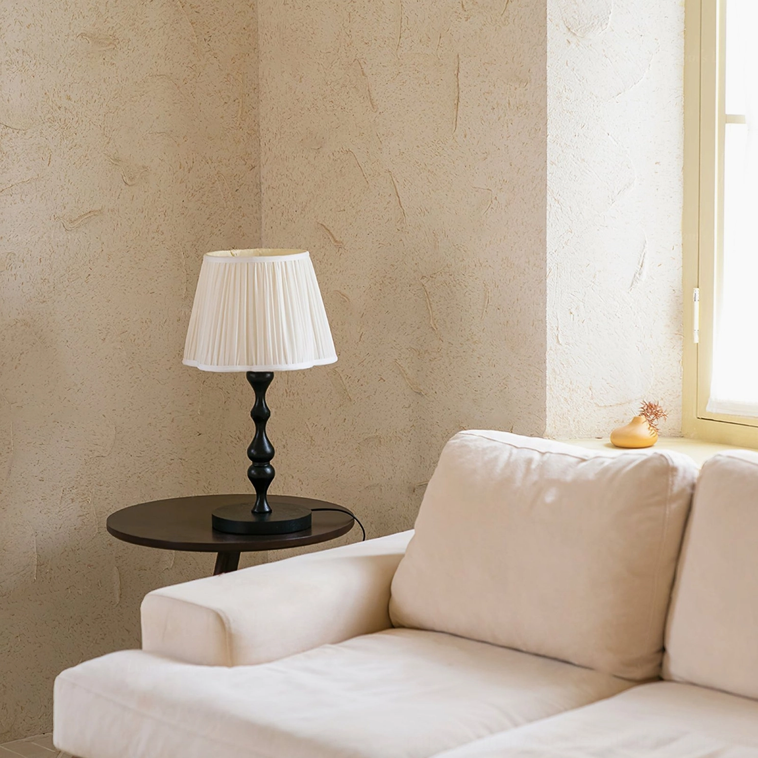 Mid-century modern table lamp with cream pleated shade and turned wooden base styled in bright living room with sofa and window