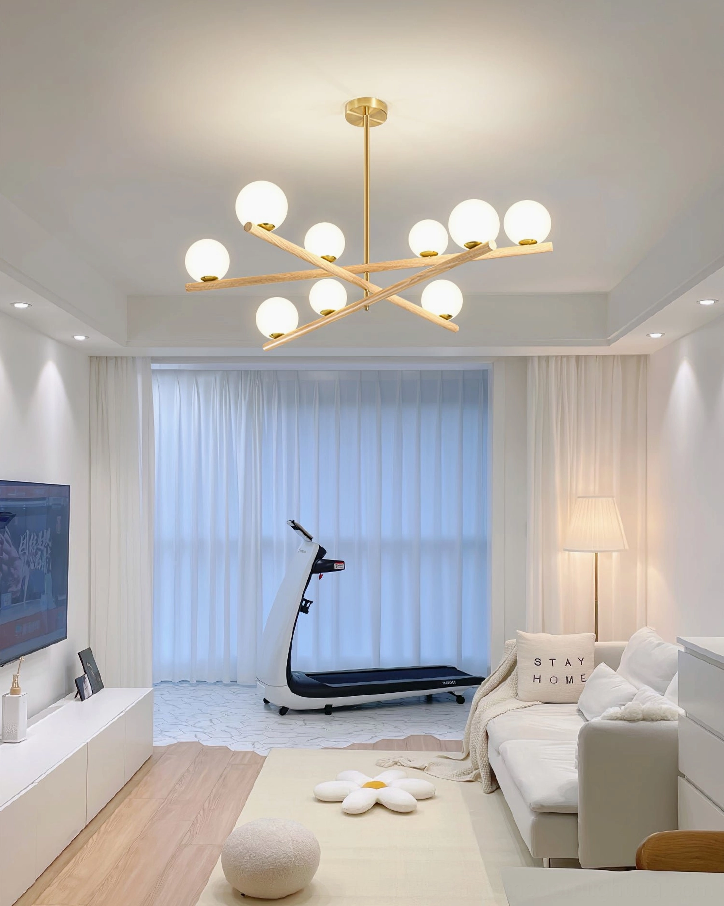 Wide-angle view of modern home with line ball chandelier in living room area next to gym space with wooden flooring