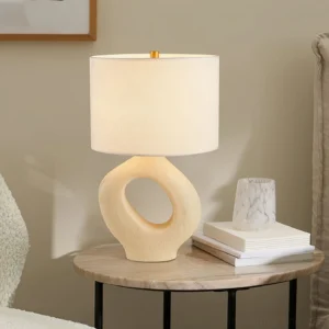 Beige hollow base Sauce table lamp displayed on side table with books and marble vessel in modern living room