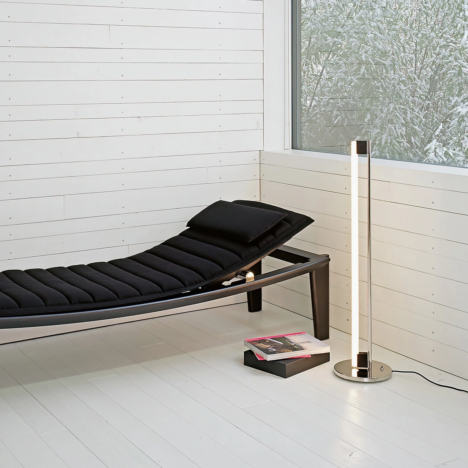 Chrome floor lamp corner positioning in minimalist lounge area with black daybed and white interior design