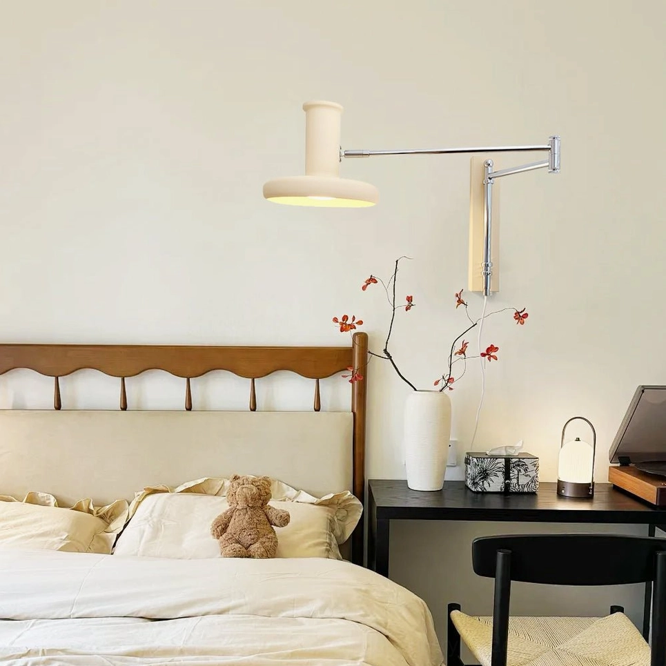 Cream colored swing arm sconce mounted on bedroom wall above side table in home study area, showing sleek metal articulated arm