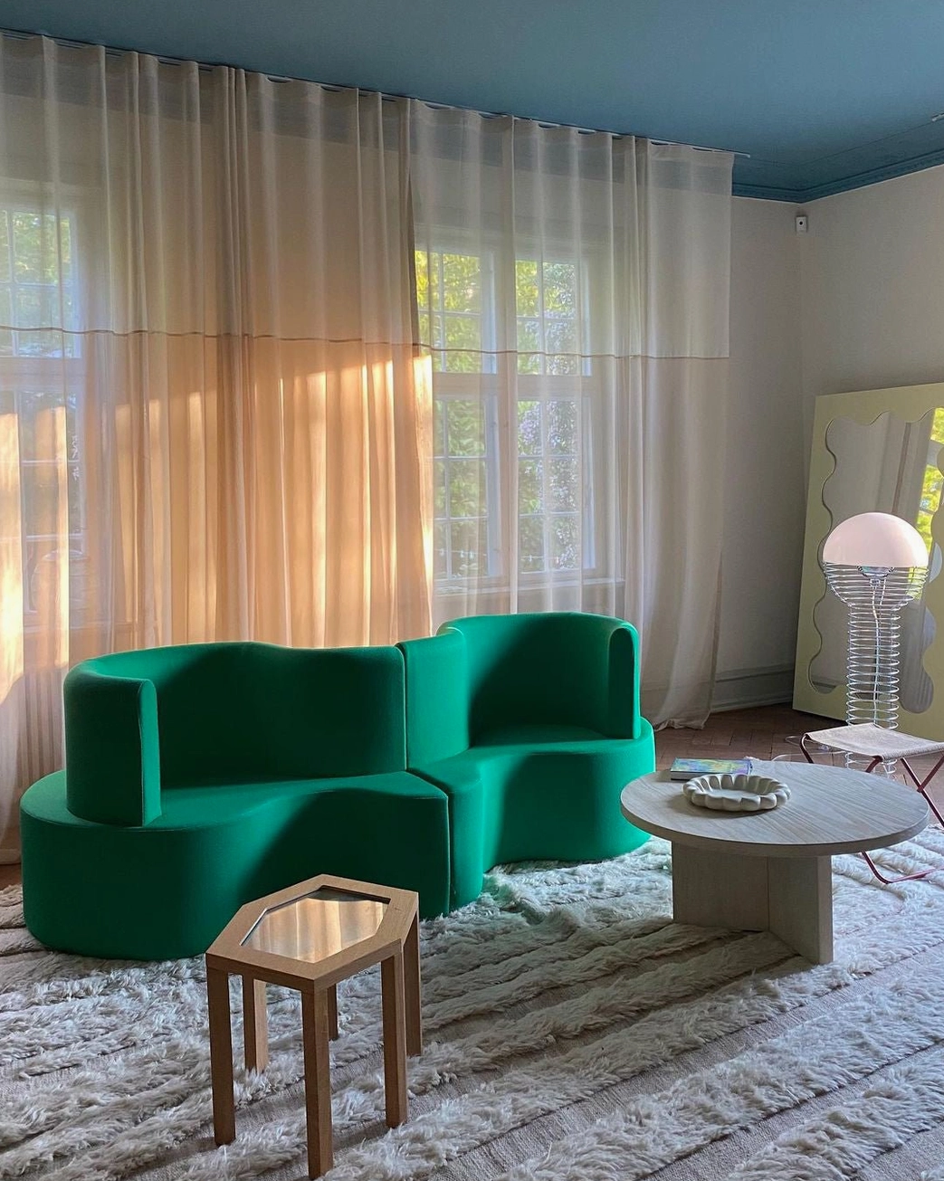 Modern wire floor lamp in bright living room with green modular sofa and sheer window curtains, contemporary design