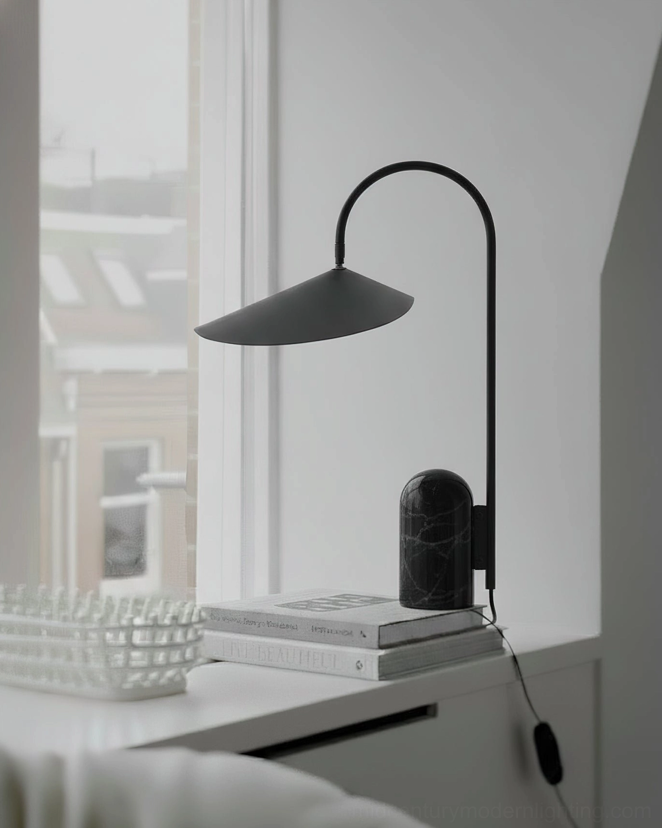 Black arc desk lamp with marble base displayed on bedroom dresser next to stacked books and natural light