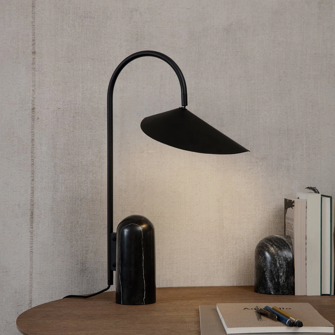 Black sculptural lamp with arched stem and marble base in modern bedroom nightstand setting