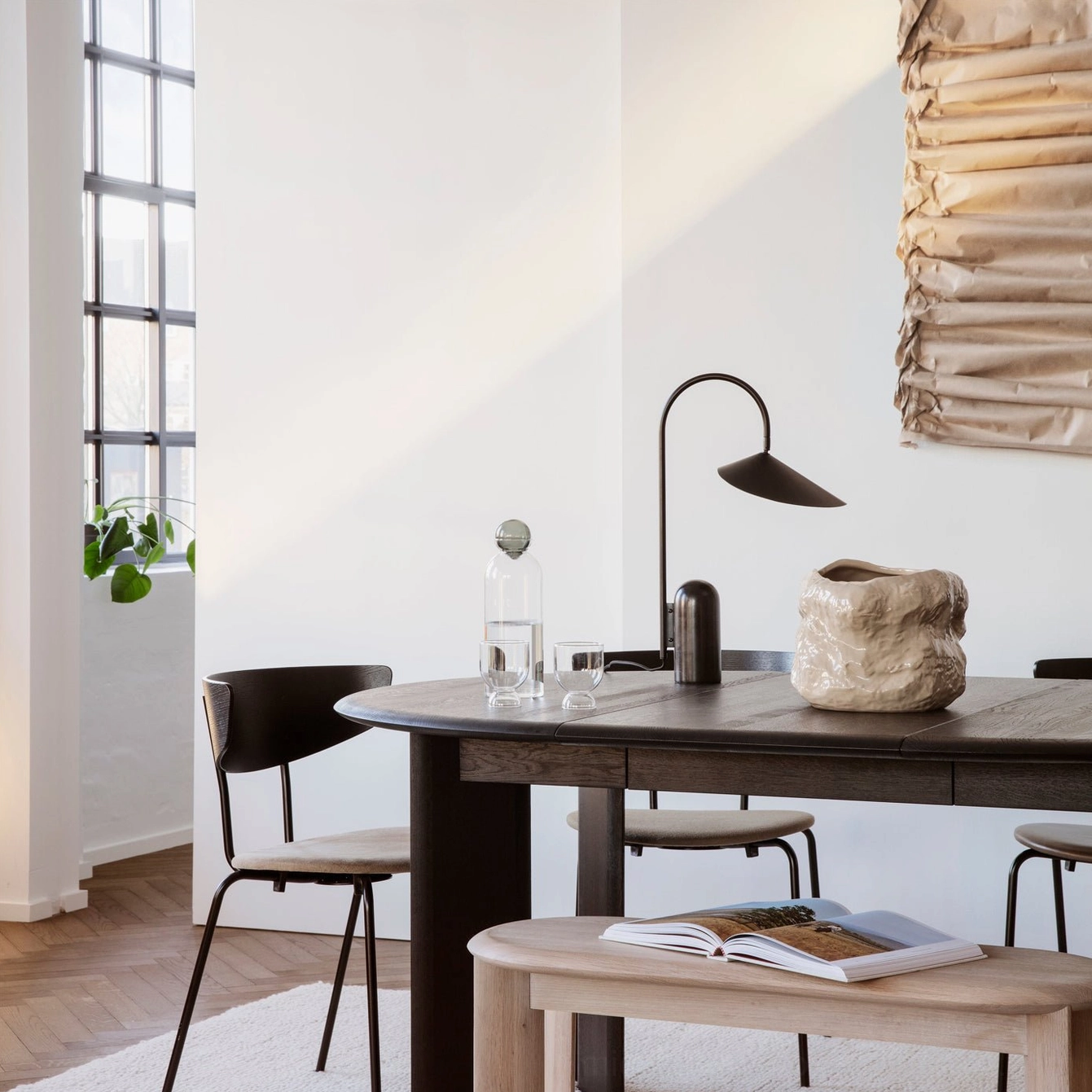 Black sculptural table lamp with arched stem on dining room table in neutral minimalist interior