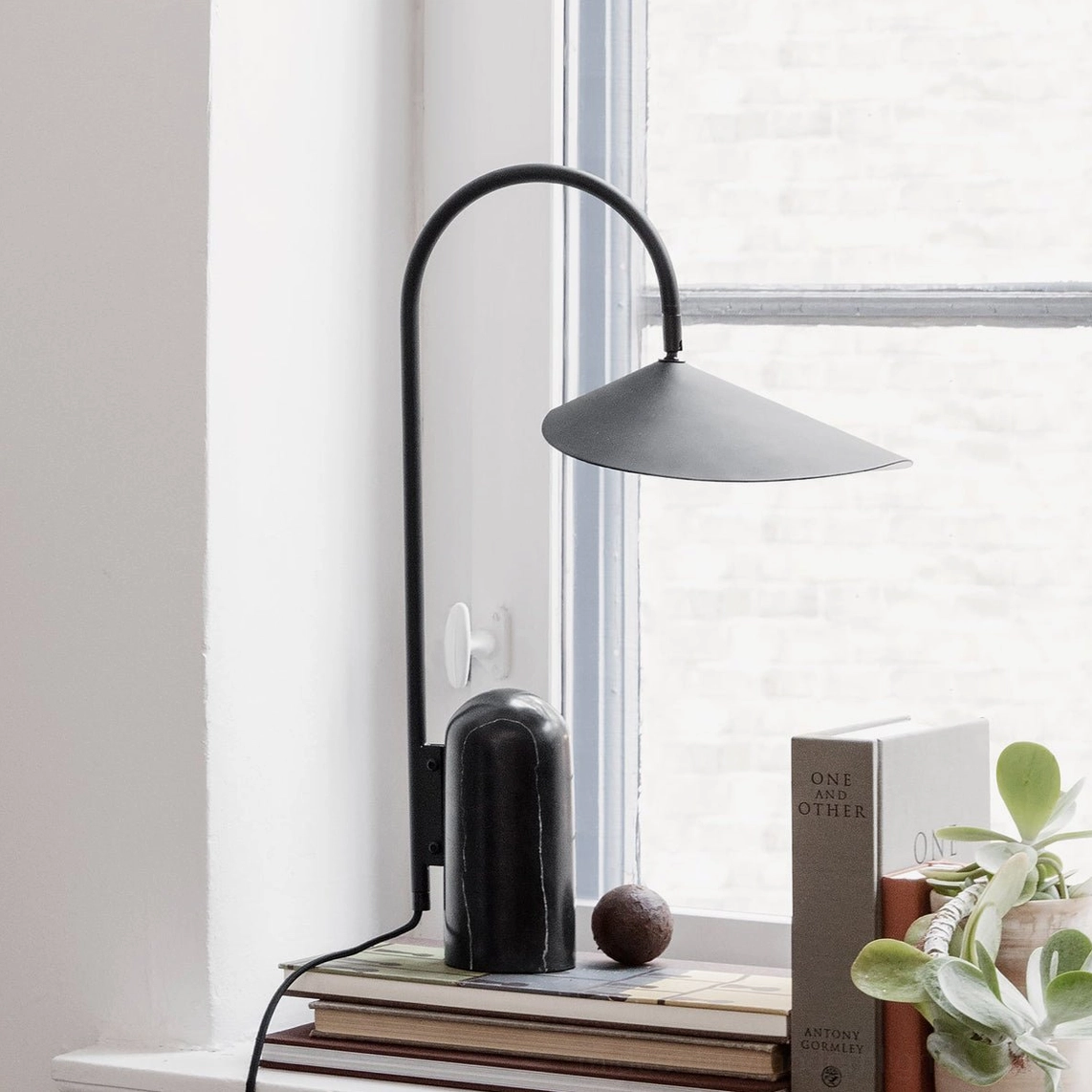 Black conical shade table lamp with arched metal stem on modern desk by window in home office