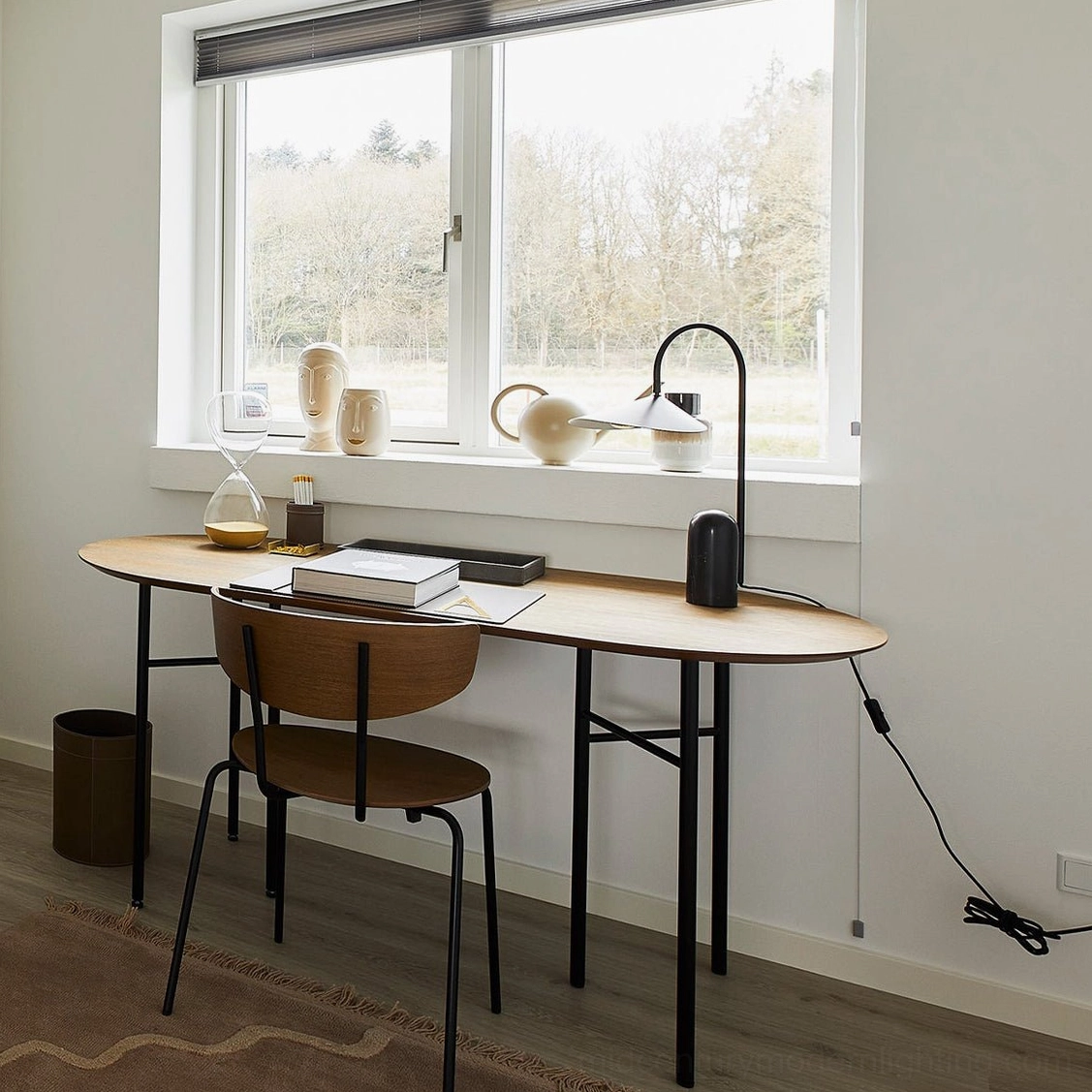 Minimalist black marble base table lamp positioned on wooden office desk with books and desk accessories
