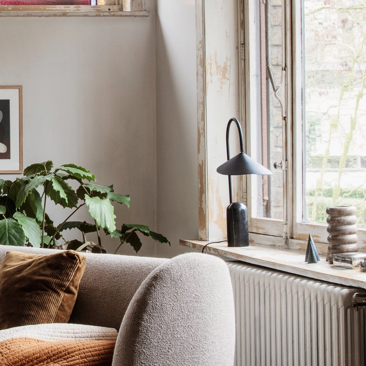 Compact black arc table lamp on radiator windowsill with minimal home accessories and warm interior