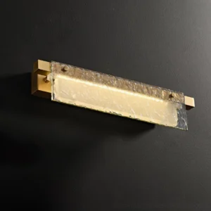Monrou wall sconce illuminated with warm light, three-quarter side view showing brass mounting and glass diffuser