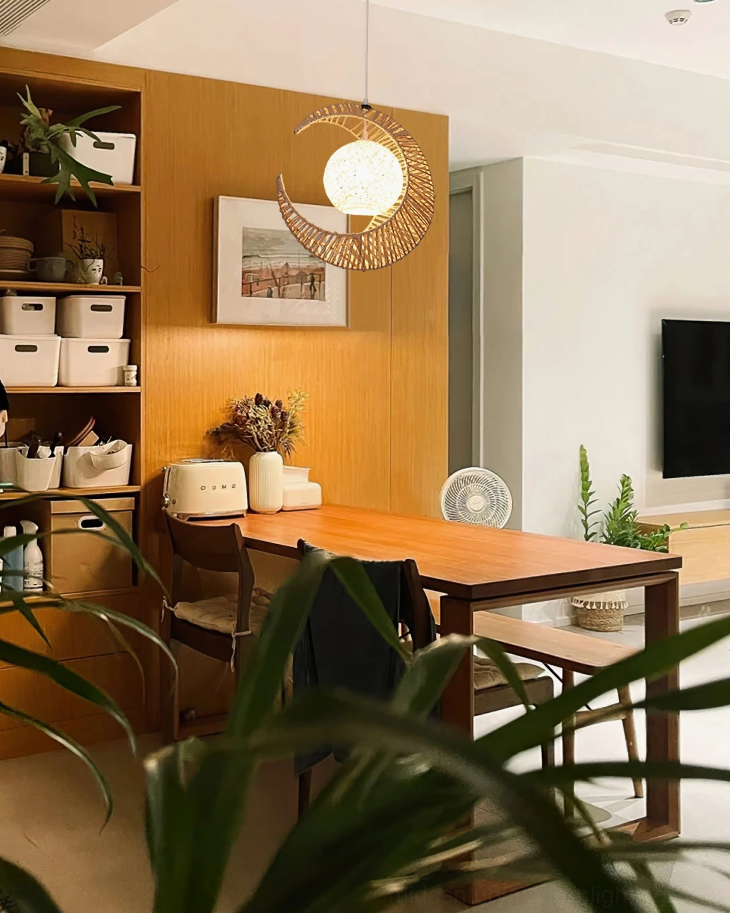 Crescent moon pendant lamp providing warm lighting over wooden dining and home office combination area