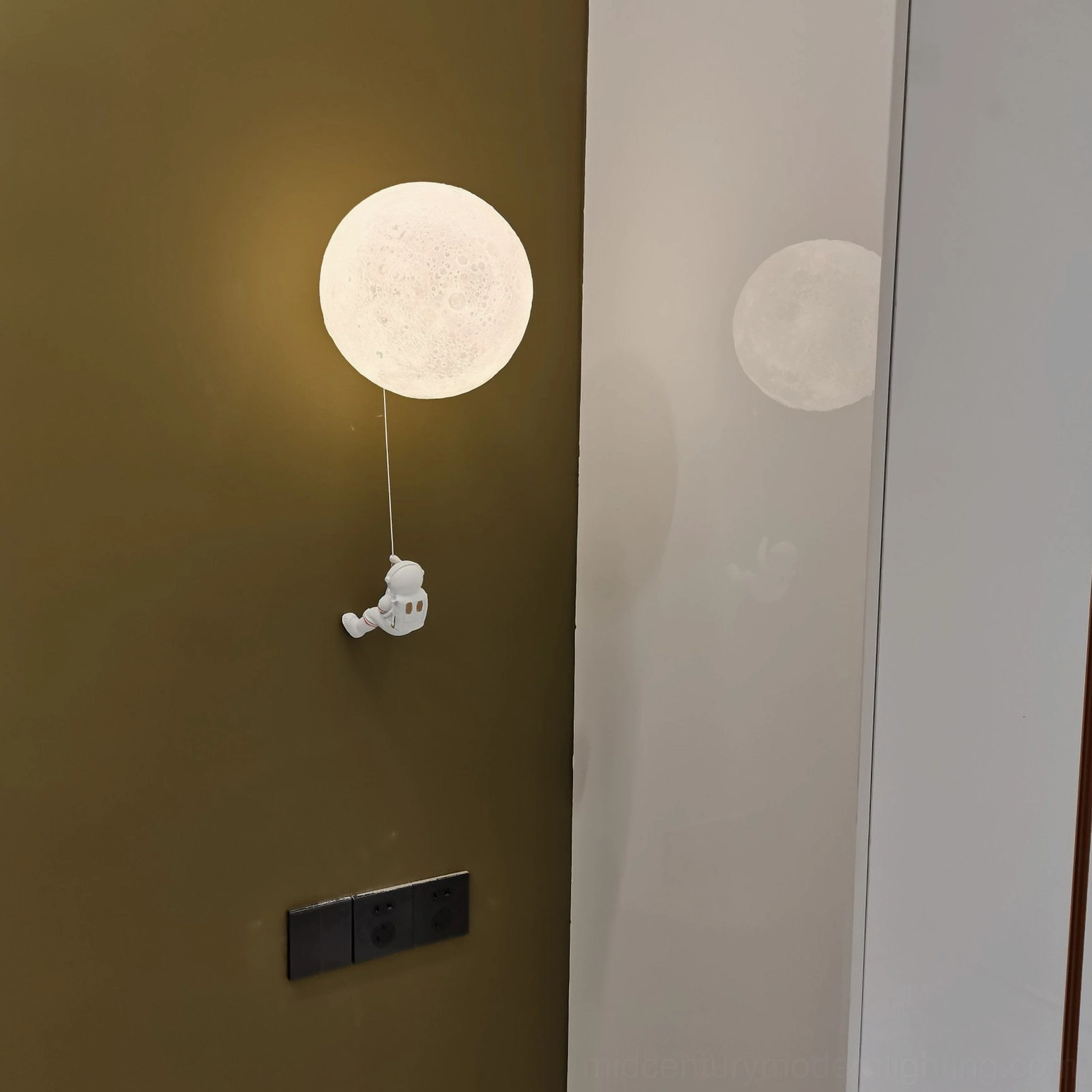 Contemporary lunar wall lamp unlit with small white astronaut decor on green wall with mirror