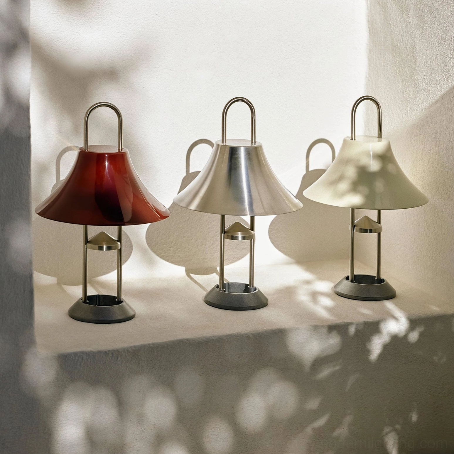 Set of three Mousqueton battery lamps in burgundy red, stainless steel, and oyster white on sunlit indoor ledge
