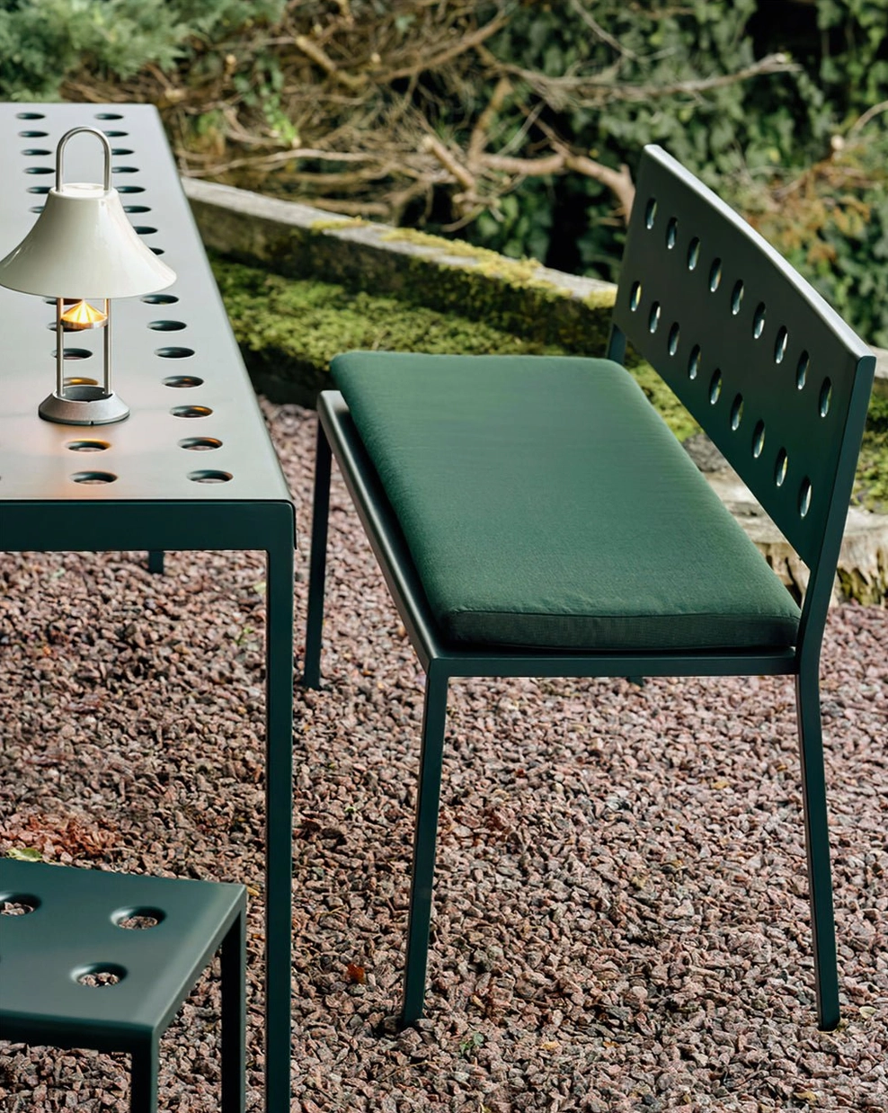 Illuminated Mousqueton cordless lamp casting warm glow in garden dining area surrounded by green outdoor decor