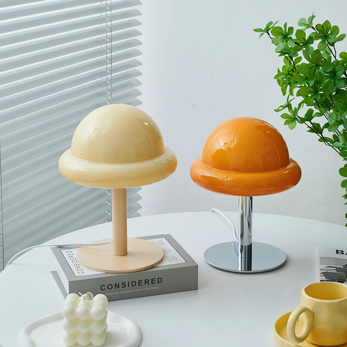 Two color variant mushroom table lamps beige and orange displayed side by side on home tabletop with decorator books