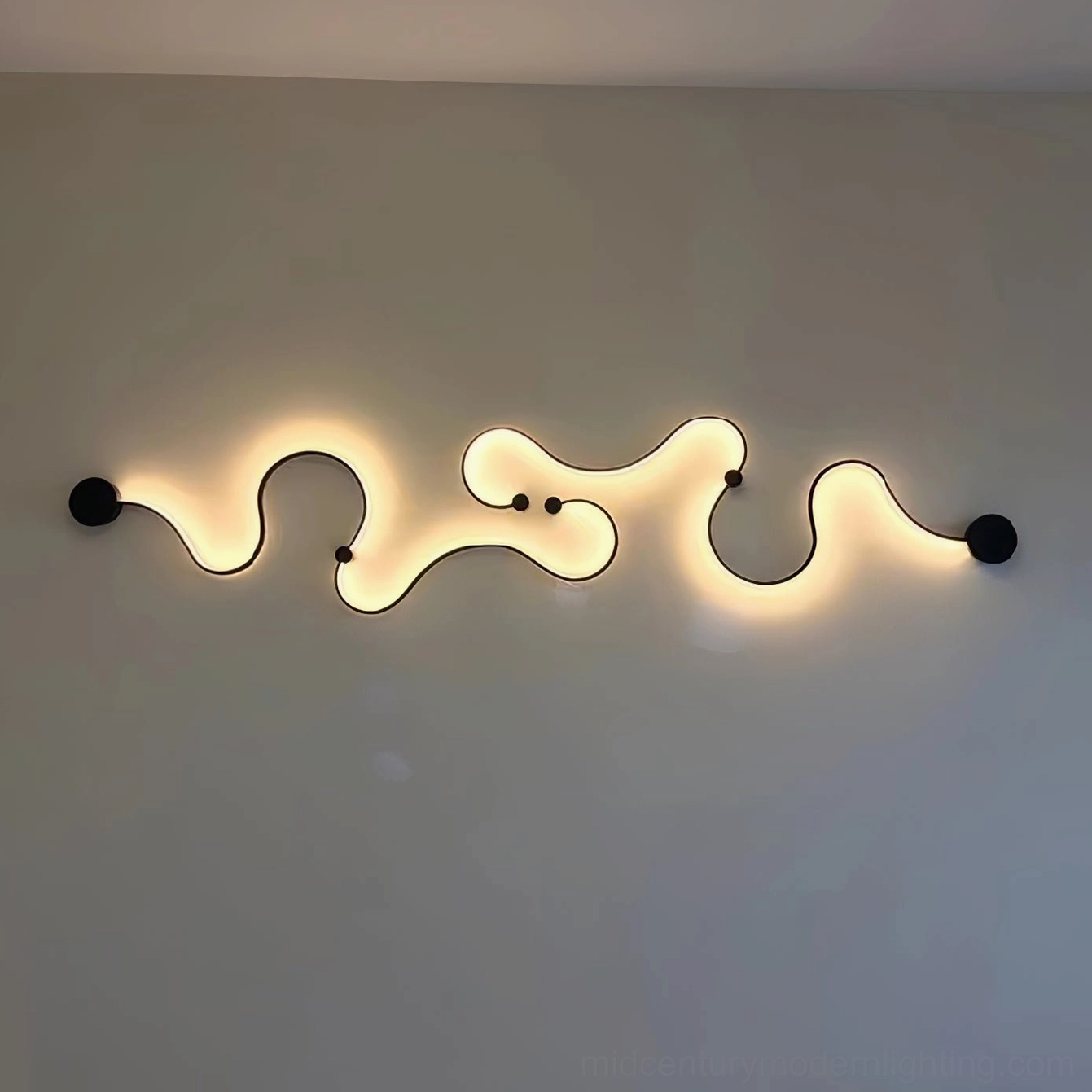 Multi-segment wavy snake wall lamp glowing warm light on gray wall background
