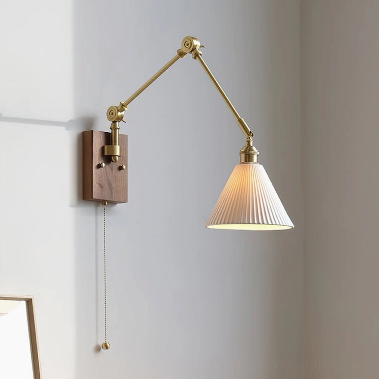 Model B murale swing arm wall lamp with brass arm fully extended, warm illuminated pleated ceramic shade against interior wall