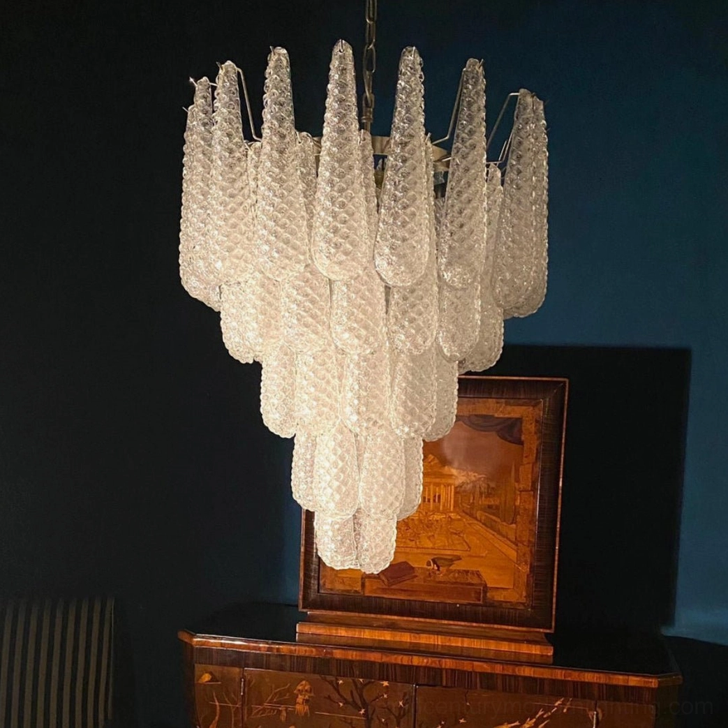 Unlit white Murano glass chandelier with faceted clear glass pendants displayed against dark vintage wall with art and cabinet