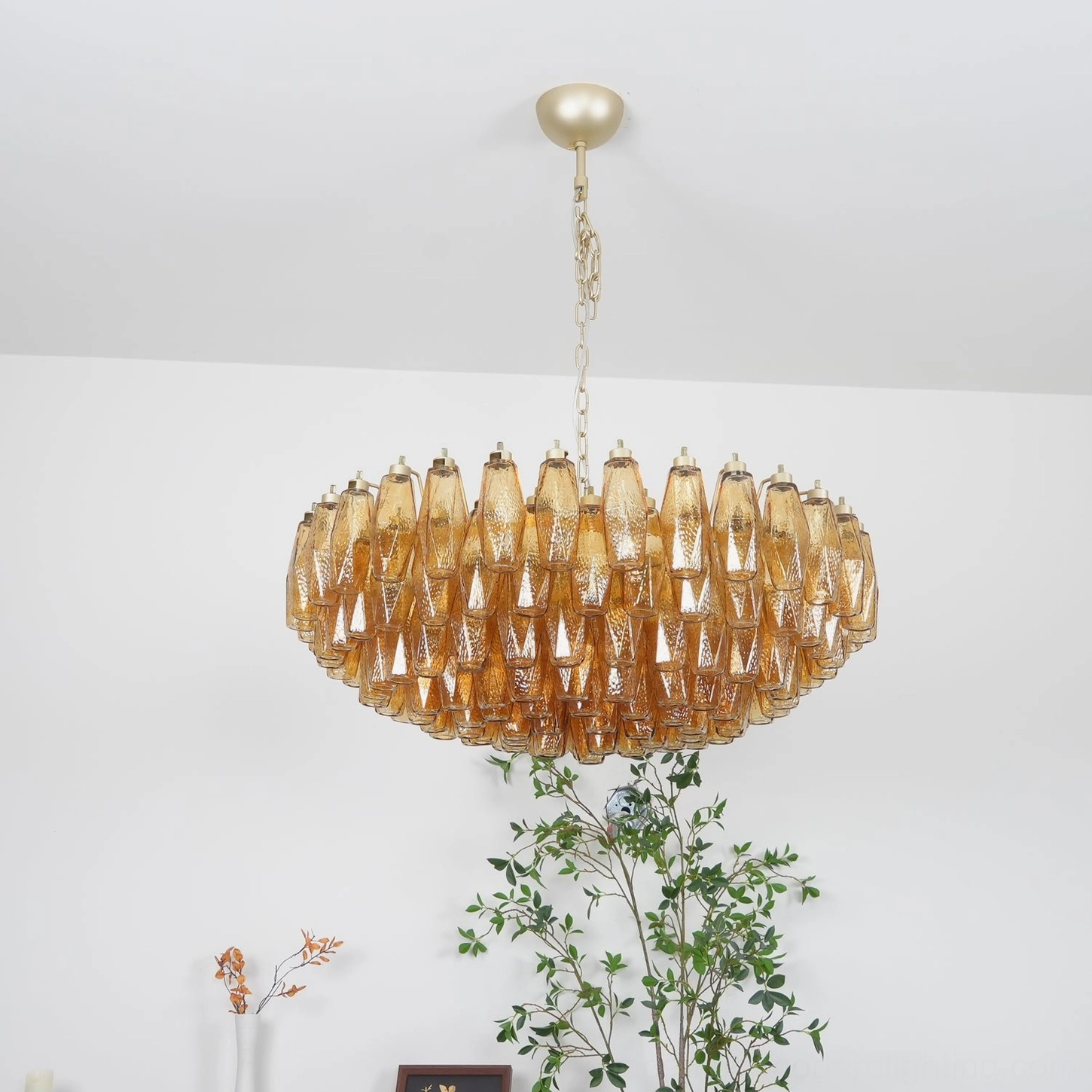 Amber glass chandelier from above showing gold metal chain and canopy with ridged glass droplets on white wall background