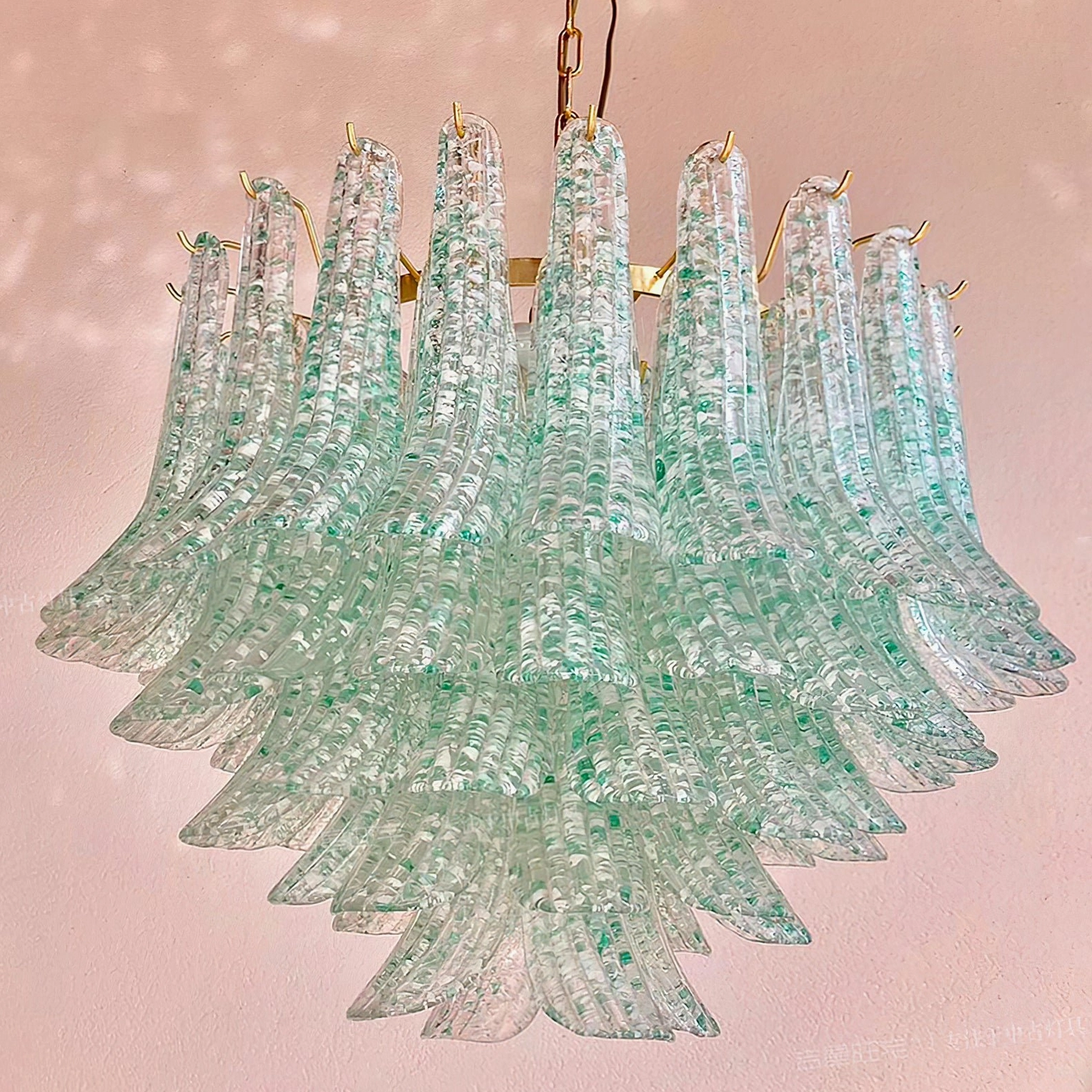 Multi-tiered Murano green chandelier with fluted glass and green speckles against pink studio background, front flat view of gold metal frame
