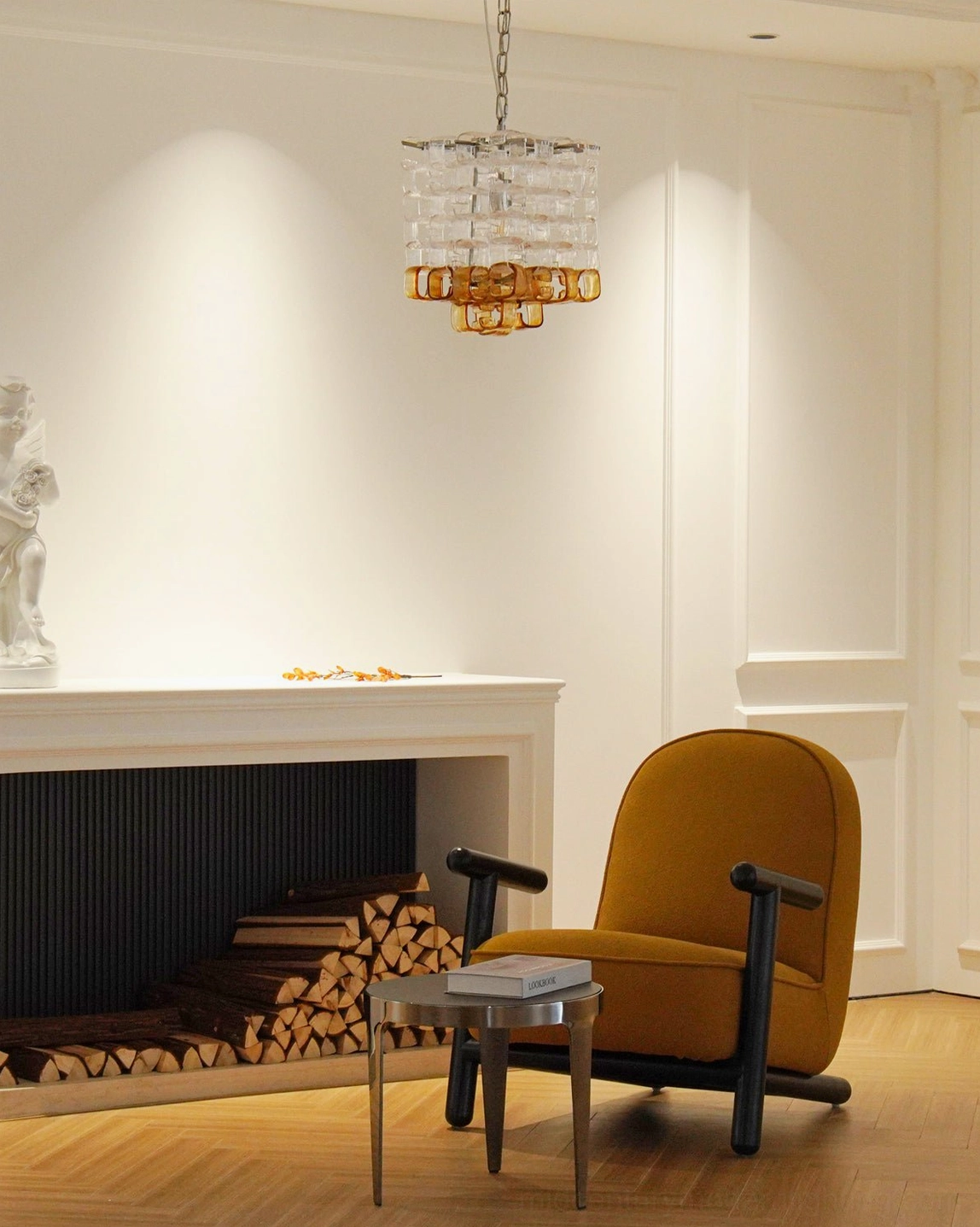 Small hanging Elodie Murano chandelier in warm-tone minimalist living room above round side table with books and neutral styling