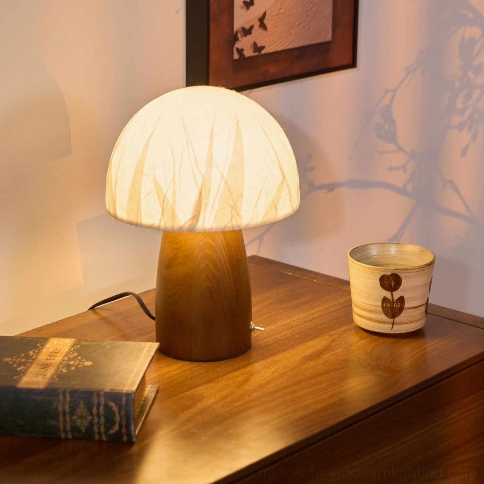 Mushroom lamp frontal three-quarter perspective on wooden dresser with vintage books and wall art