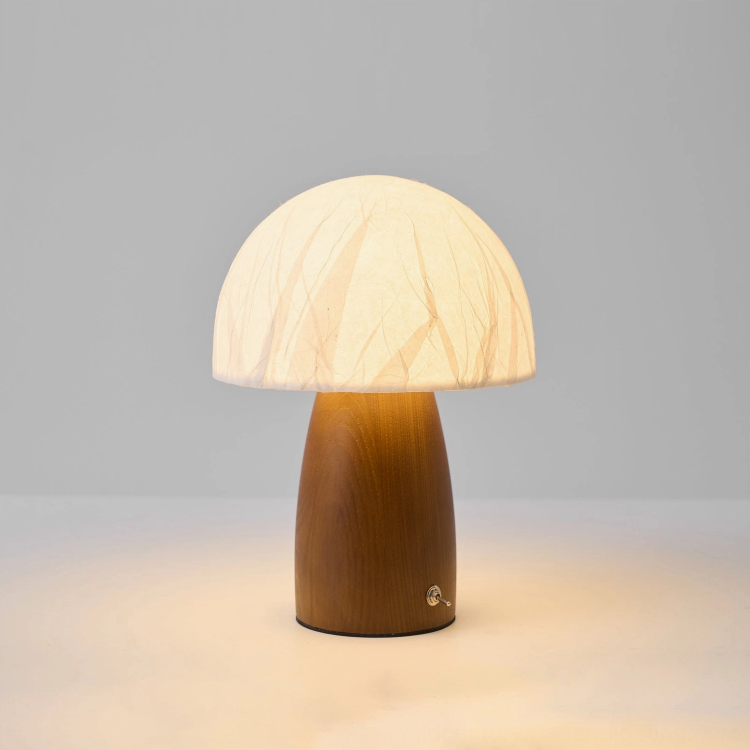 Lit mushroom table lamp with warm glow, crinkled paper shade, dark brown wooden base on white background