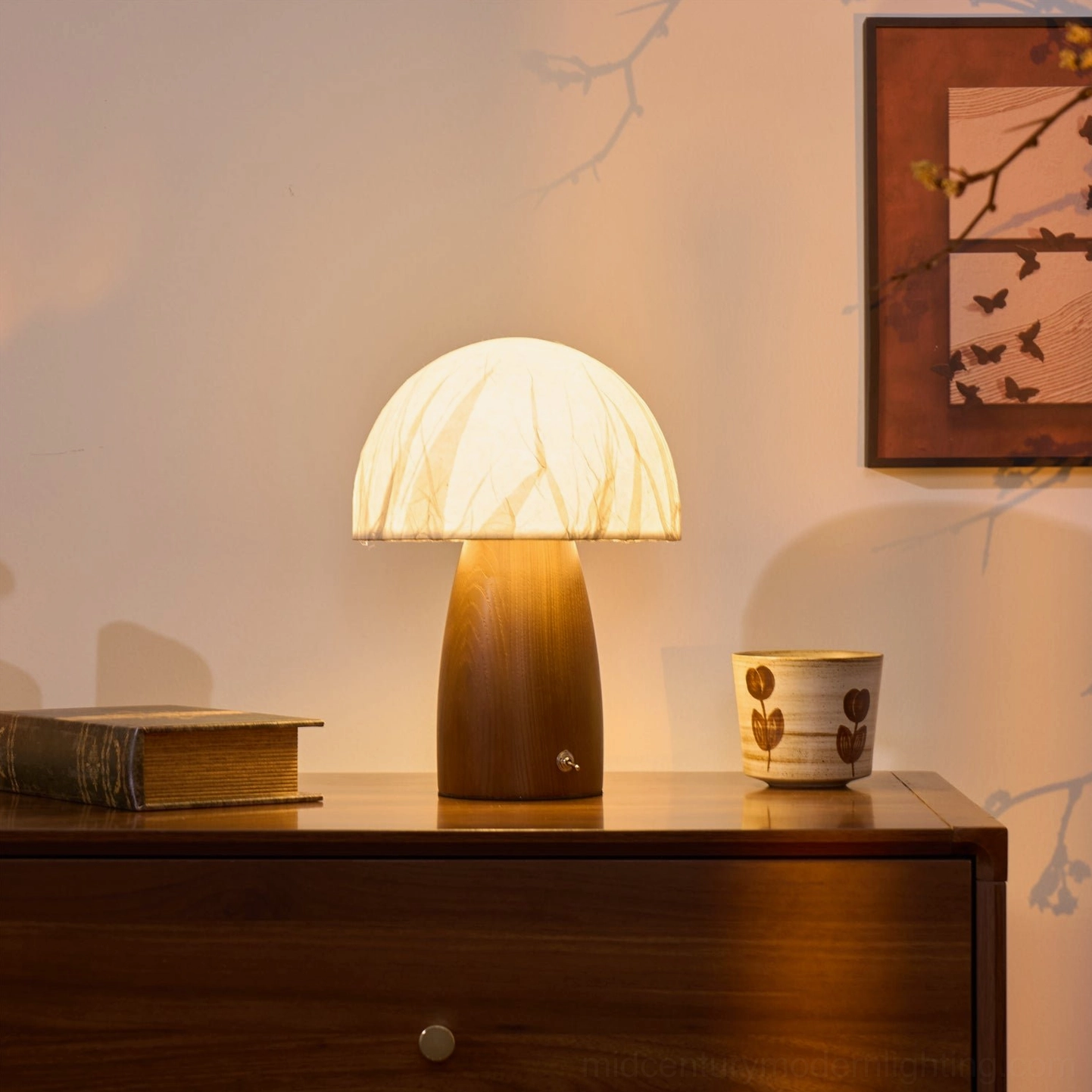 Side three-quarter view of mushroom lamp on wooden dresser with branch shadow and ceramic cup decor