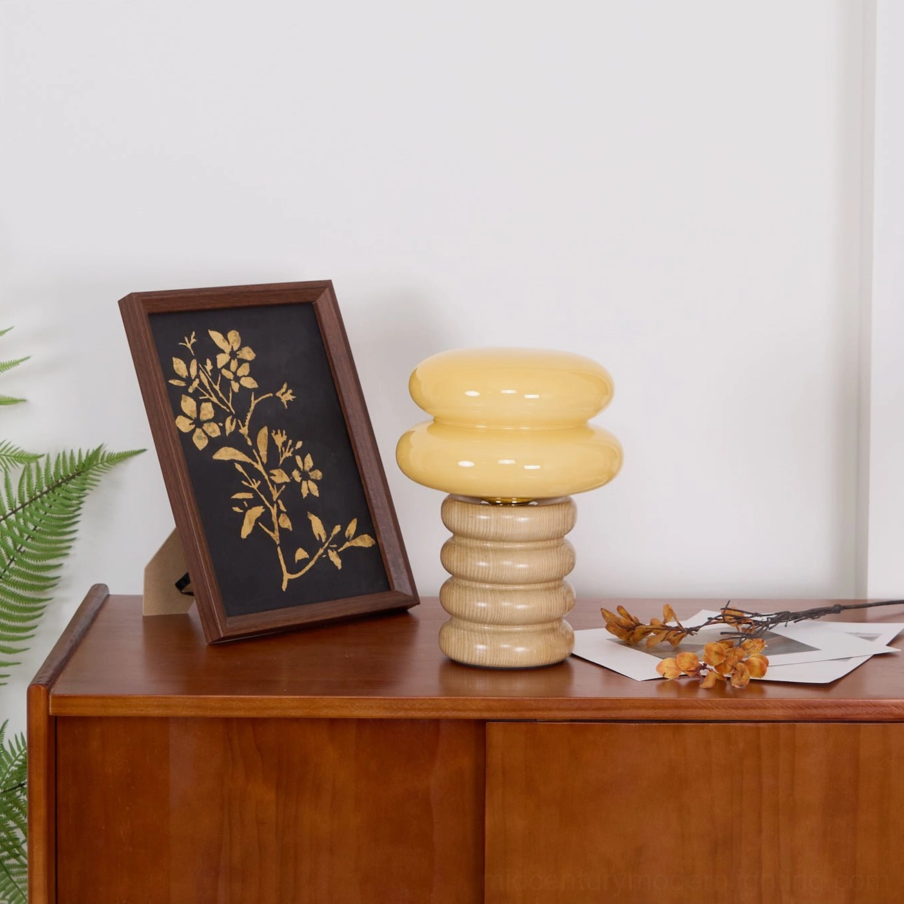 Cozy home vibe with compact Napako stacked table lamp on sideboard surrounded by framed art and green foliage accessories