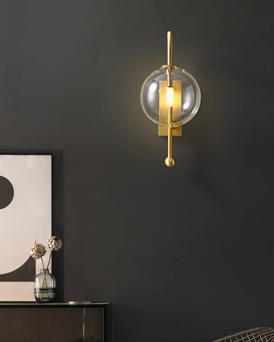 Minimalist wall sconce with square brass backplate and hanging glass ball on dark accent wall