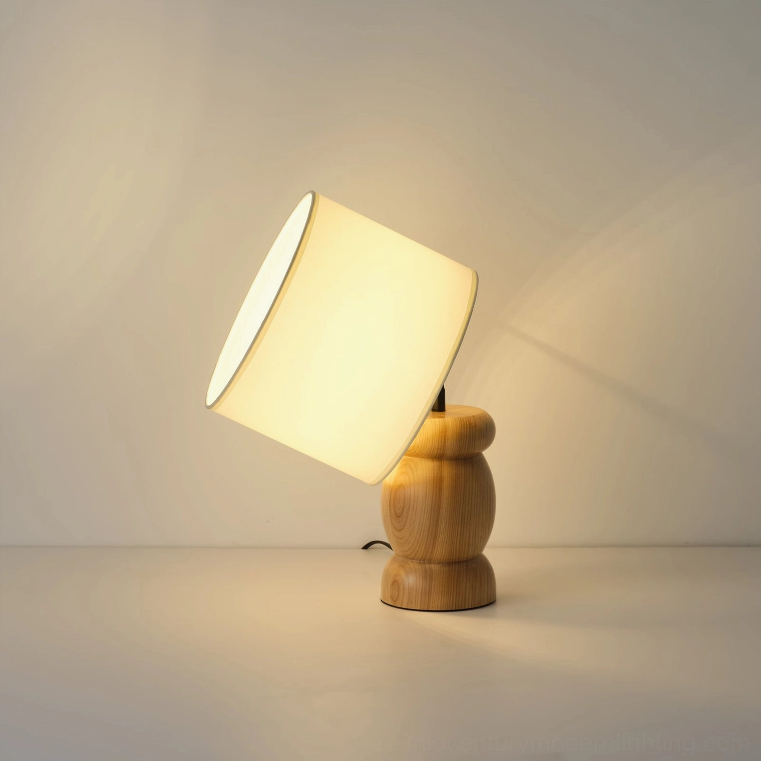 Natural wood base table lamp with fabric shade, three-quarter perspective showing warm lighting, mid-century craftsmanship