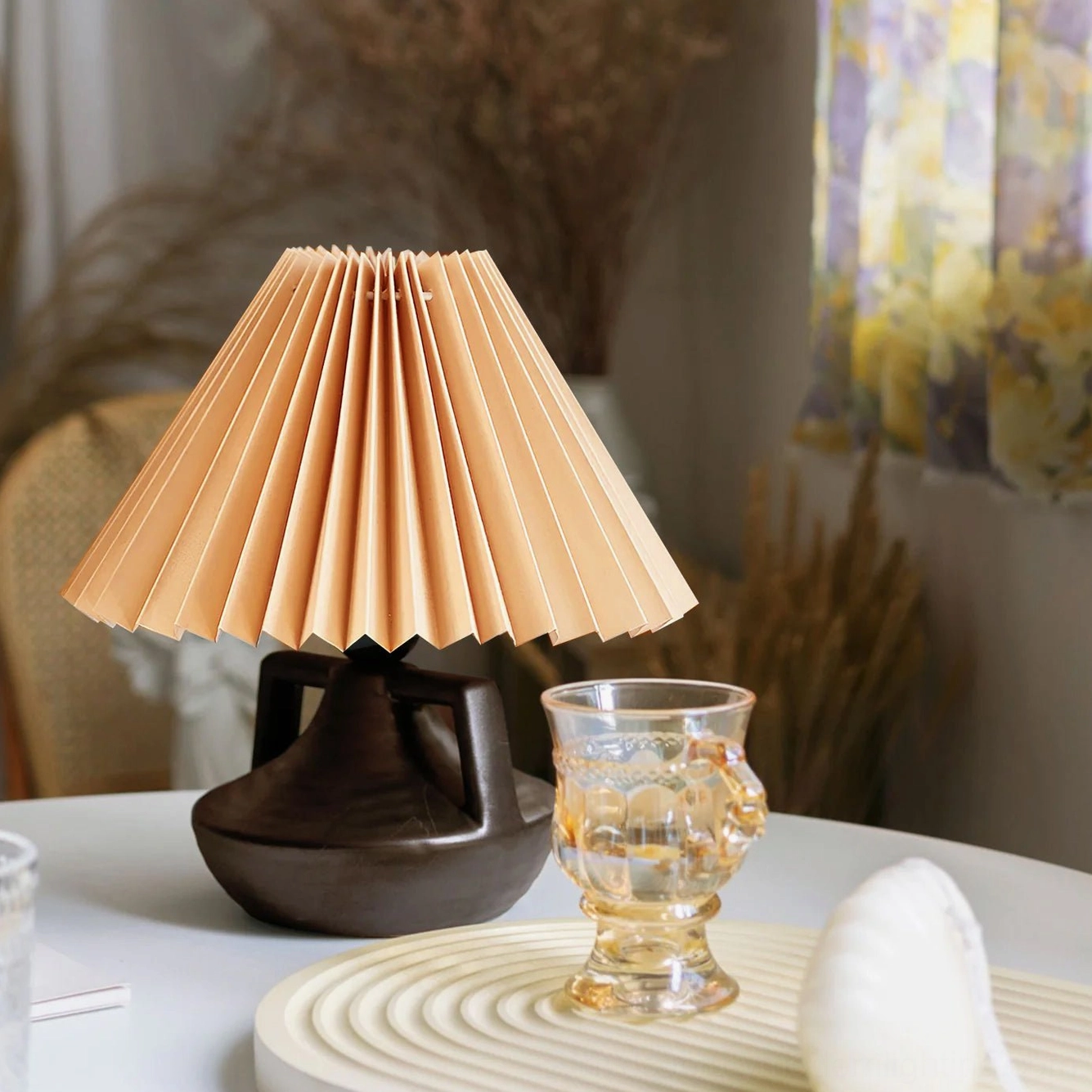 Navia ceramic pleated lamp on table with glassware and decorative tray, warm vintage tabletop